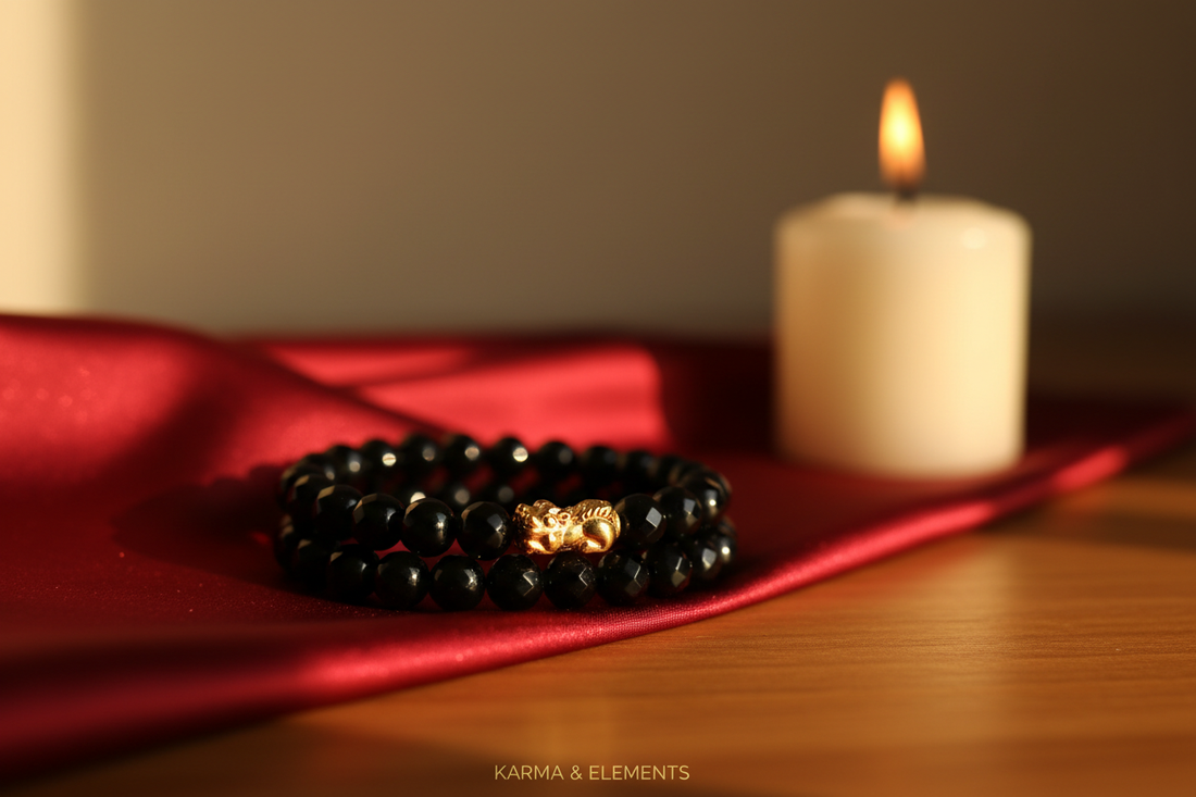 Black obsidian Pi Xiu Feng Shui bracelet on red silk with a candle in warm amber light — Karma & Elements